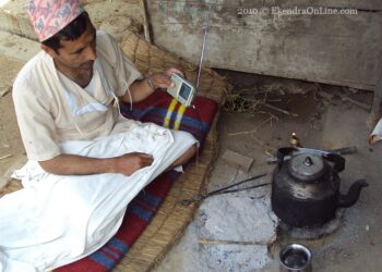 Man listening radio by the side of his outdoor kitchen & bed in a village in rural Nepal; communication is everywhere!