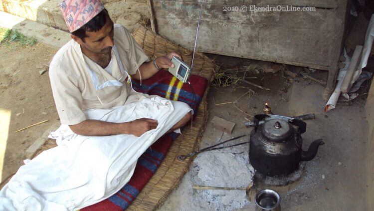 Man listening radio by the side of his outdoor kitchen & bed in a village in rural Nepal; communication is everywhere!